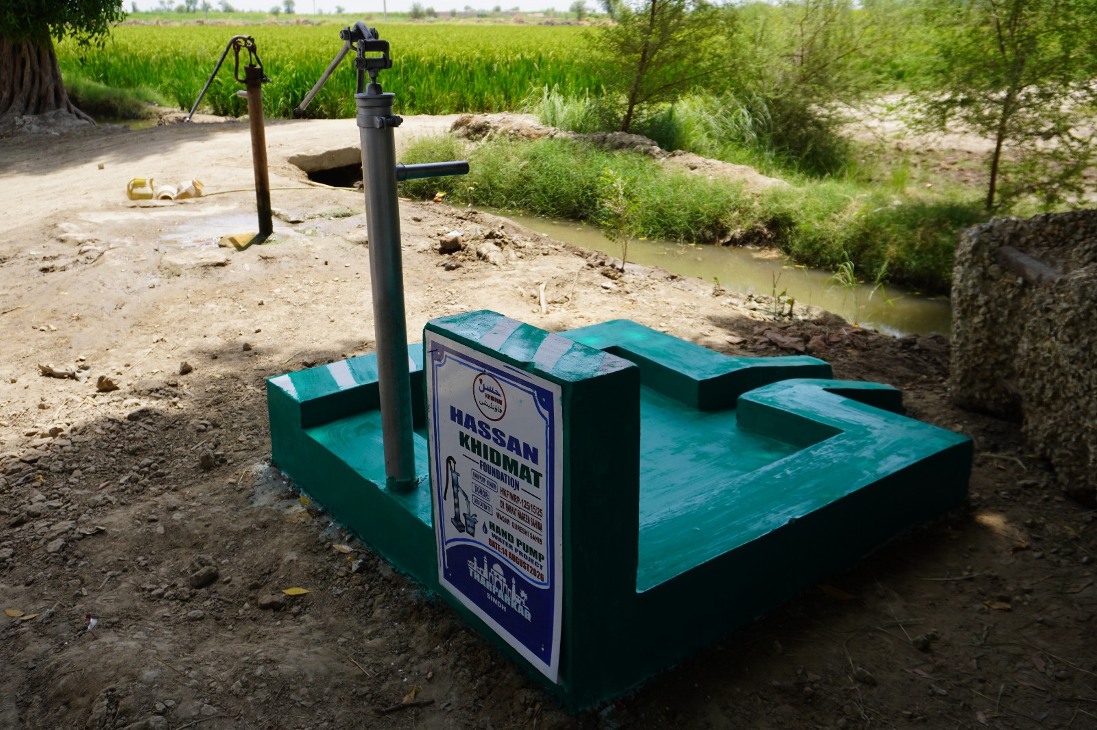 Completed green hand pump beside agricultural fields